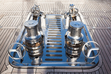 Teak deck of a luxury yacht with stainless steel winches and anchor chain attachment mechanisms.