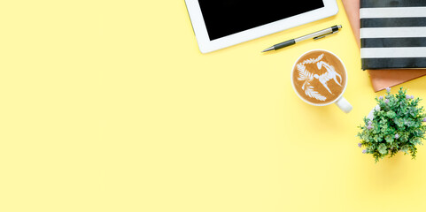 Office desk with tablet, pen, notebook, Cup of coffee on yellow background, Top view with copy space, Mock up..