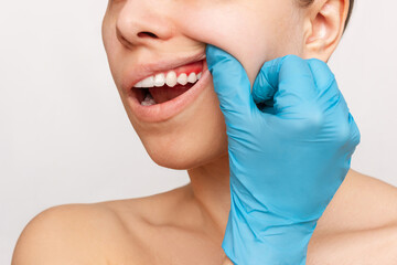 Gum inflammation. Cropped shot of a young woman's face with doctor's hand in blue glove on her jaw...