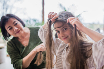 Grandmother helping her little granddaughter with making a hairstyle.