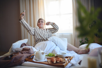 Happy overweight woman with taking selfie when having breakfast in bed at home.