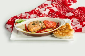 Baked salmon fillet with pita bread, cucumber, tomato in a dish isolated on colorful table cloth top view on grey background
