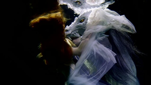 an elegant young woman is submerged under the water, she is wearing a beautiful dress from the Middle Ages. a dragon floats nearby like in a fairy tale.