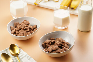 Nougat bites - sweet cocoa and hazelnut wheat puffed pillows - breakfast cereal in white bowls, glasses with milk on sunny orange background