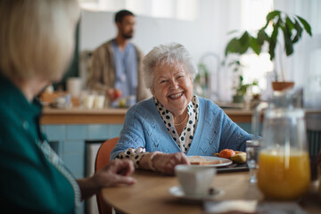 Smiling elderly woman enjoying breakfast in nursing home care center.