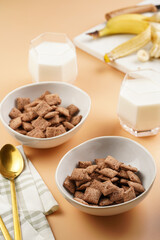 Nougat bites - sweet cocoa and hazelnut wheat puffed pillows - breakfast cereal in white bowls, glasses with milk on sunny orange background