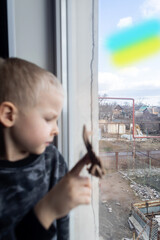 Russian attack on Ukraine. Child sits on the window and cries. Against the background of a destroyed building, cracks and devastation near. Consequences of hostilities and the shelling of civilians