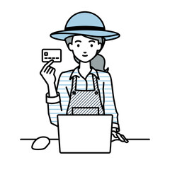 デスクで座ってPCを使いながらクレジットカードを手に持っている農家の女性