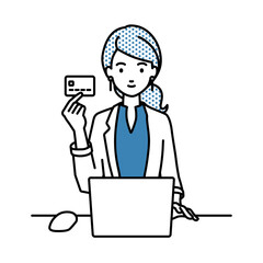 デスクで座ってPCを使いながらクレジットカードを手に持っているジャケットの女性