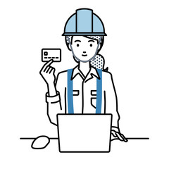 デスクで座ってPCを使いながらクレジットカードを手に持っている工事現場の女性