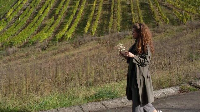 Portrait of a beautiful, stylish, happy hipster woman walking on a vineyard, playing with an autumn wreath and enjoying sunshine. Female happiness, romantic thoughts and freedom in nature concept. 4K