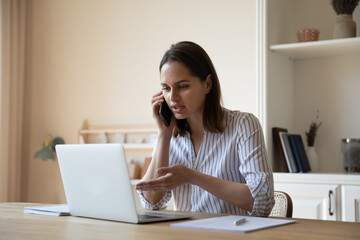 Woman looks at laptop makes order on-line, talks to sales manager on smartphone, discuss purchase, buy remotely, work from home office, negotiates, answers questions provide assistance on phone call