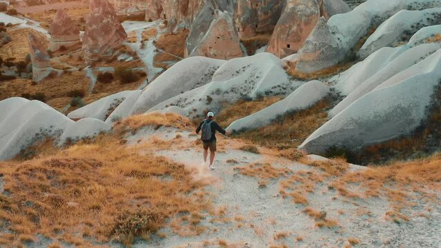 Drone follows happy free tourist man with backpack hiking, running down sandy mountain path to enjoy epic view panorama. - Powered by Adobe