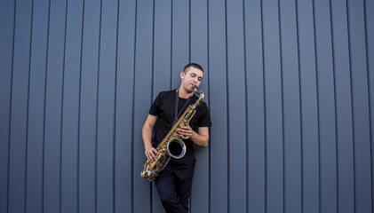Young street musician playing saxophone near the big blue wall