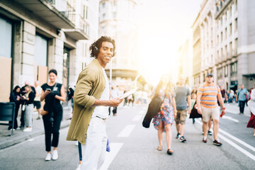 Half length portrait of cheerful male blogger in bluetooth headphones crossing city road and...