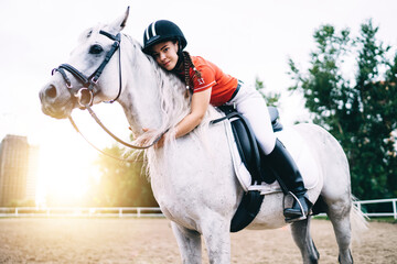 Portrait of carefree female rider sitting at saddle horseback and hugging lovely mare animal during...
