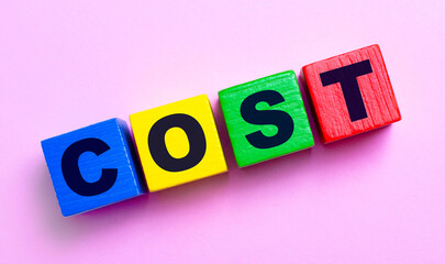 On a light pink background, multi-colored wooden cubes with the text COST