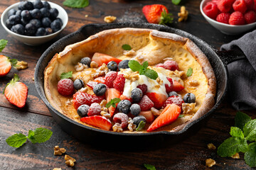 Dutch baby pancake with berries and icing sugar in a iron cast pan. Morning breakfast