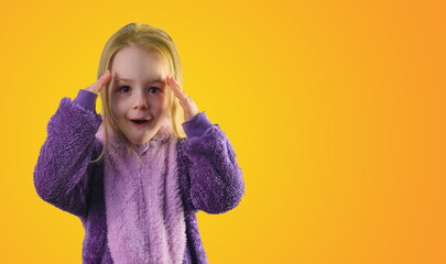 surprised little toddler girl in pajamas hands on her head yellow background