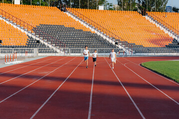 A large group of boys ' children are taught by a coach at the start before running at the stadium during sunset. A healthy lifestyle.