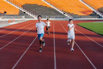 Fototapeta premium A large group of boys ' children are taught by a coach at the start before running at the stadium during sunset. A healthy lifestyle.