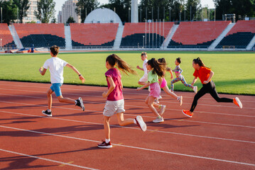 A large group of children, boys and girls, run and play sports at the stadium during sunset. A healthy lifestyle.