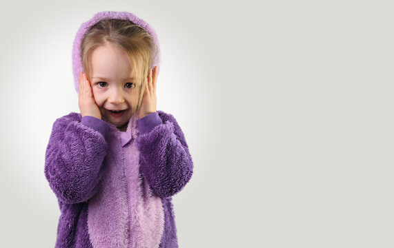 surprised little child in purple pajamas hands on her head isolated on yellow 