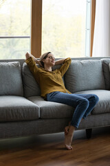 Vertical view serene woman relax on sofa with eyes closed and hands behind head enjoy carefree day...