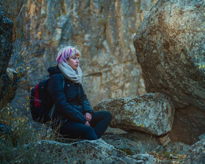 Tranquilidad en la naturaleza, chica joven sentada en medio de la naturaleza, mujer con pelo rosa y mochila sentada entre rocas