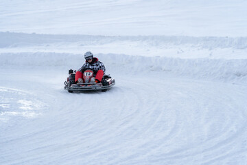 Fototapeta na wymiar Go karting on icy track in winter. Young adult karting driver in action on outdoor icy track