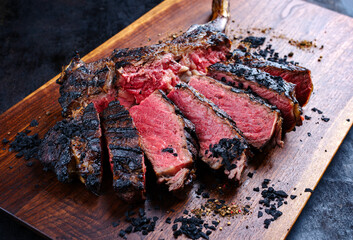 Modern style barbecue dry aged Chianina tomahawk steak sliced and served as close-up on a wooden...