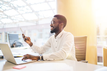Cheerful african american male office worker typing on laptop computer working online checking...