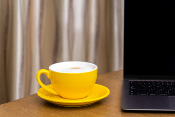 Yellow coffee cup and Laptop computer on wooden table