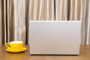 Yellow coffee cup and Laptop computer on wooden table