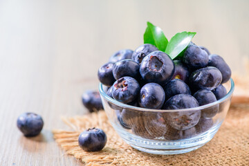 Fresh organic blueberries in a glass bowl on wood background,