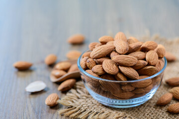 Almonds nut with leaves in glass cup on wood background.