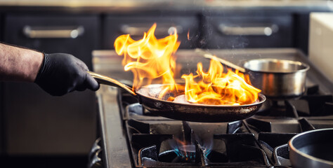 Pro chef flambeing in the kitchen in a pan on a gas-fired stove