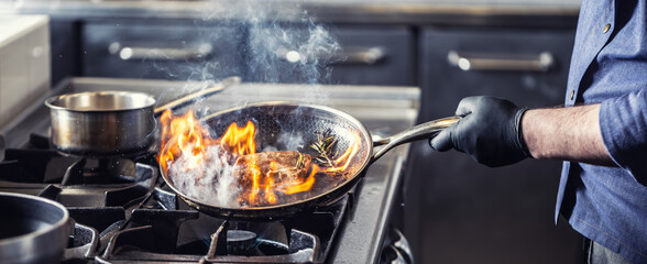 Chef in the kitchen leans pan to the side for alcohol in it to catch fire for gas stove, starting...