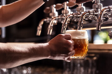 Woman hands of the pub employee tapping beer into a rounded mug.