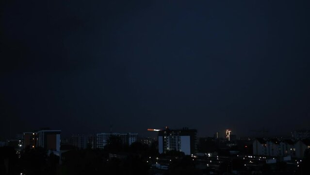 Thunderstorms, lightning over city. Flash strikes in stormy night falling on buildings in city. Lightning thunderstorm flashes over the night sky. Low key lighting. Underexposed. Blue light