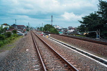 Fototapeta na wymiar A railroad track made of iron, wood and gravel in a suburban area on a cloudy day in Indonesia