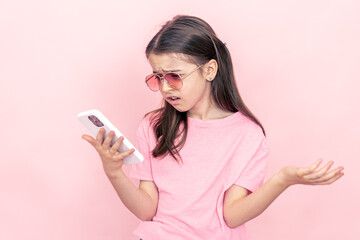 Fototapeta premium Stylish little girl with a smartphone on a pink background.
