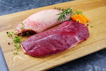 Traditionelles rohe Gourmet Entenbrust Filets mit Haut angeboten mit Kräutern und Orangenscheibe als close-up auf einem Holz Design Board