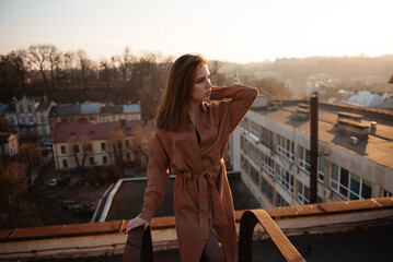 Young woman in dress posing on rooftop at sunset