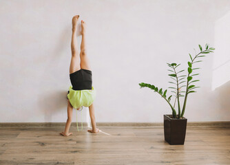Little gymnast does exercises at home. girl doing exercise near the wall.