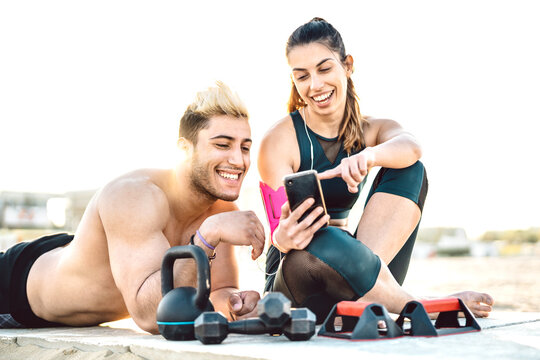 Young couple having break at sport fitness training and sharing plan on mobile smart phone - Technology sport concept with trendy sporty people enjoying moments with smartphone - Warm backlight filter