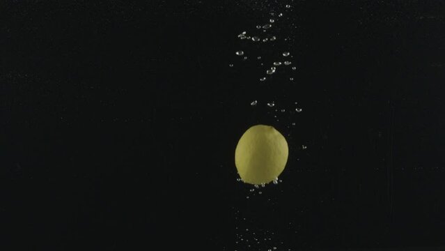 Yellow Lemons, citrus limonum, Citrus aurantifolia, Fruits falling into Water against Black Background, Slow Motion 4K