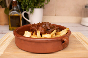 A rustic clay plate with goulash and potatoes, placed on a wooden board. Traditional foods concept.