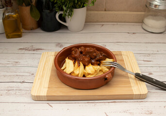 A rustic clay plate with goulash and potatoes, placed on a wooden board. Traditional foods concept.