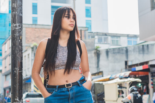 beautiful brown-skinned latina girl standing on the street in the city of Pereira-Colombia. university student thinking about her life project with her hands in her pockets while waiting for the bus.